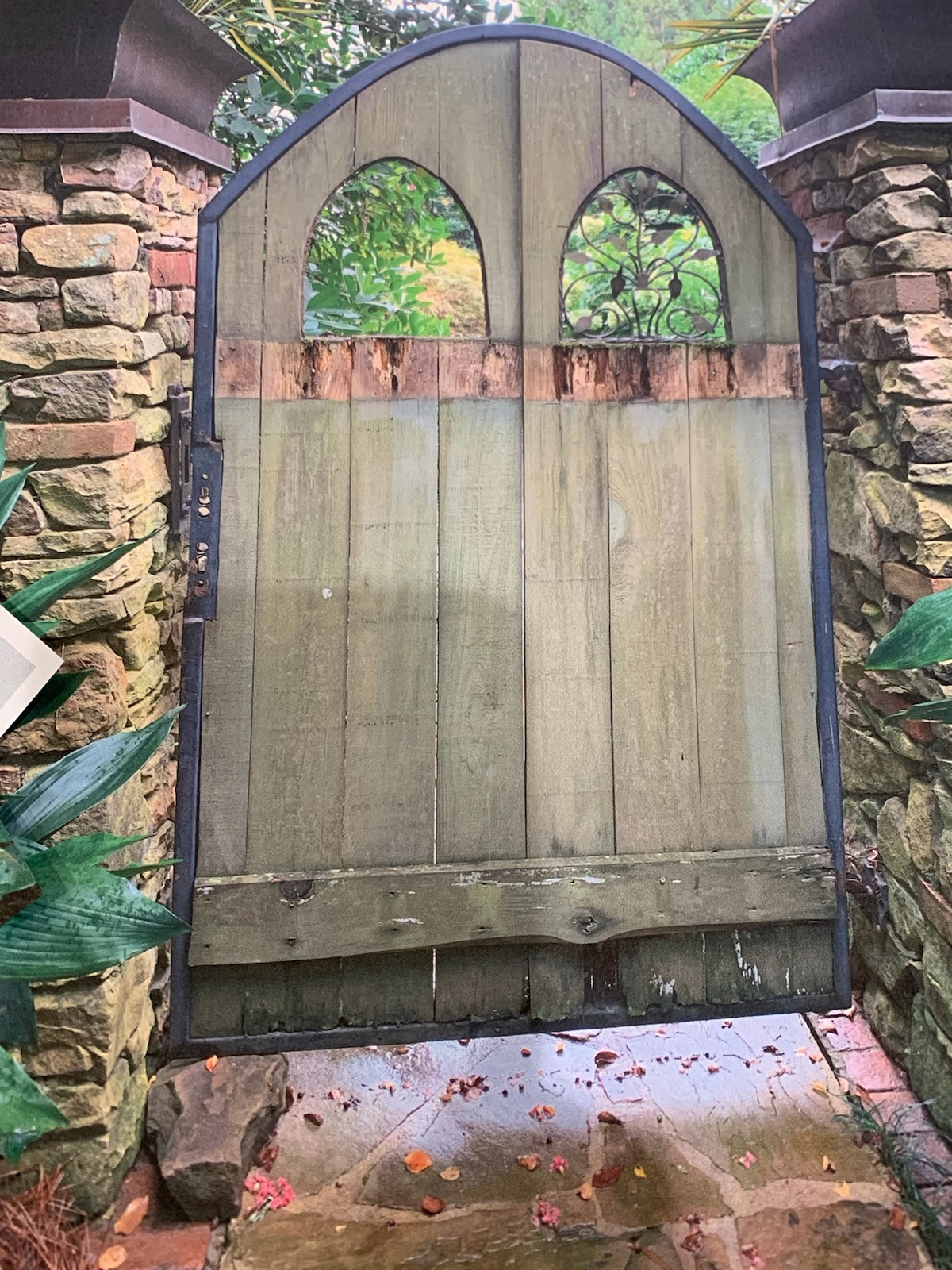 Weathered, rotting arched wood garden gate in a stone wall before rebuild