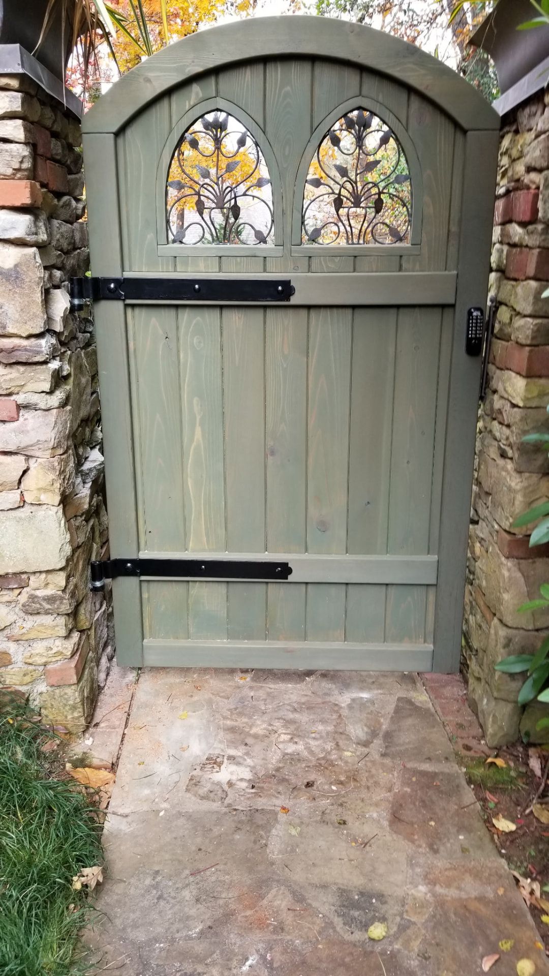 Rebuilt arched garden gate with restored ironwork, strap hinges and green exterior finish