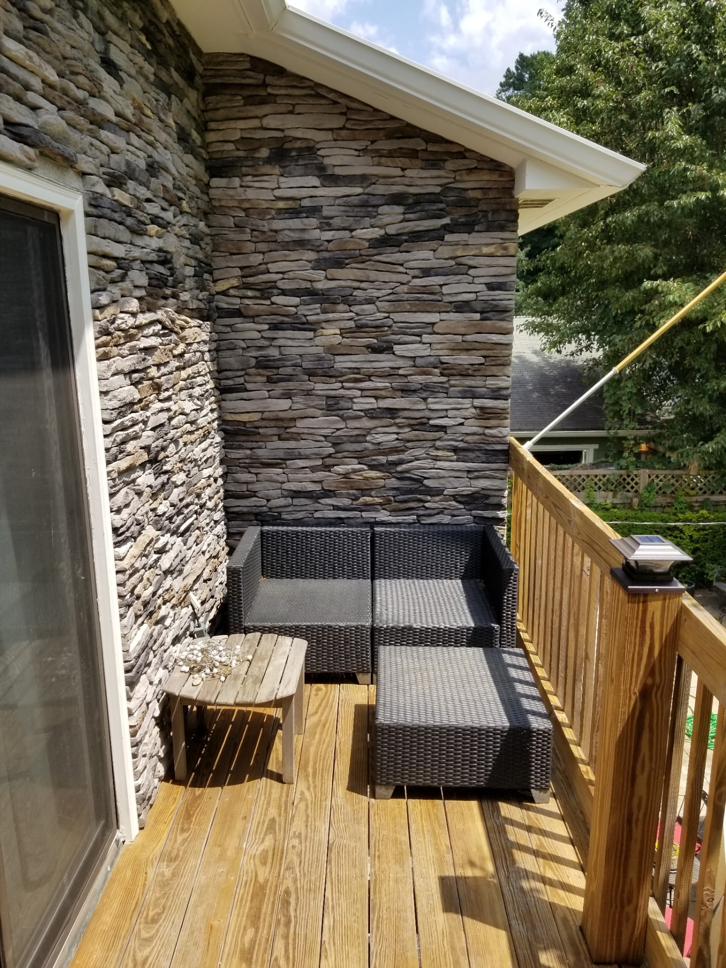 Finished wood deck with outdoor furniture beside a stacked-stone wall